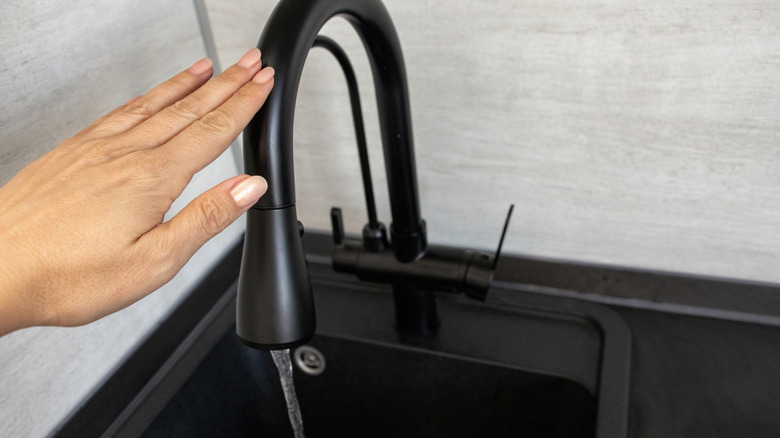 A woman places her fingers over the sensor on a black metal touchless kitchen faucet.