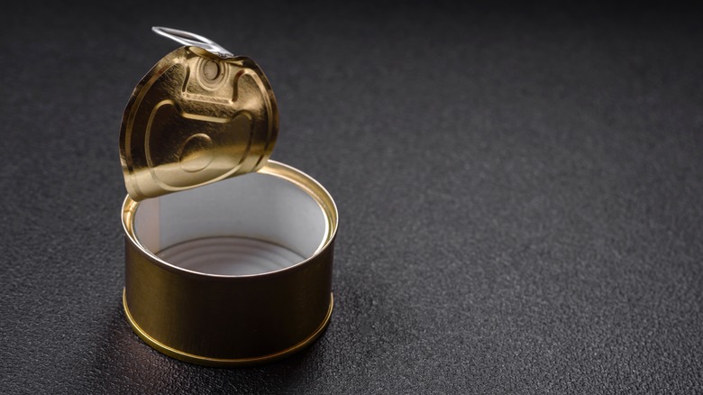 Empty gold tuna can on black textured surface