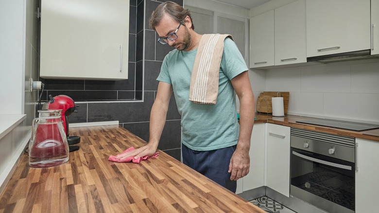 Man cleaning butcher block countertop with pink cloth