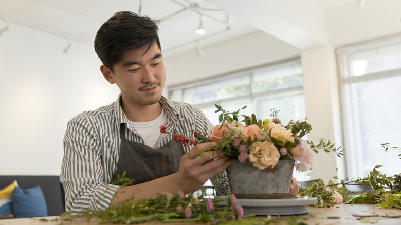 A smiling Asian man making a floral arrangement
