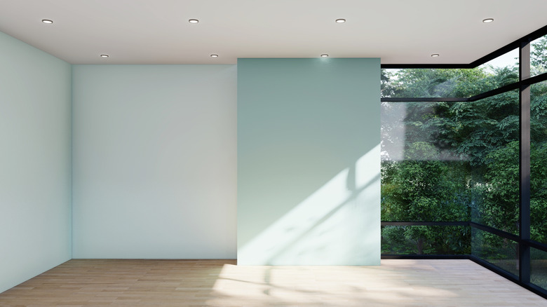 Large empty wall space in a room with pale green walls, a large, corner window, and wood floors