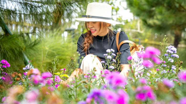 Young woman in a white hat admires colorful flowers in pink and white.