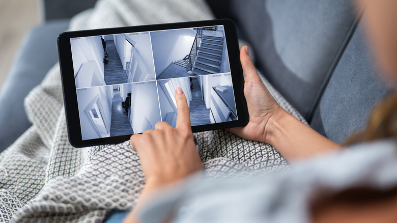 A person monitoring security cameras' live view of home via a digital tablet.