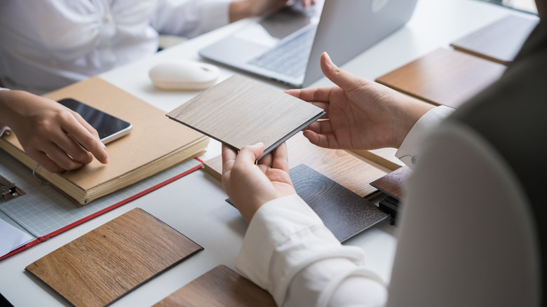 Person showing flooring sample to another person across a table