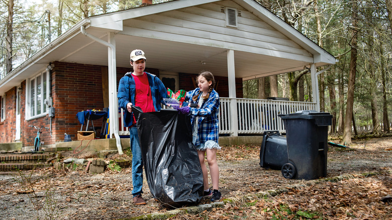 Young man holding trash bag while girl puts trash in it
