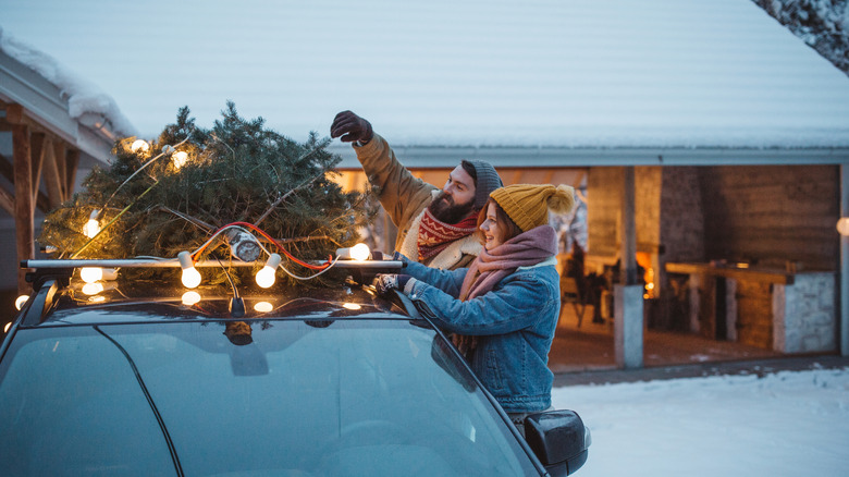 A coupe unties their Christmas tree on the top of their car to take it inside their home.