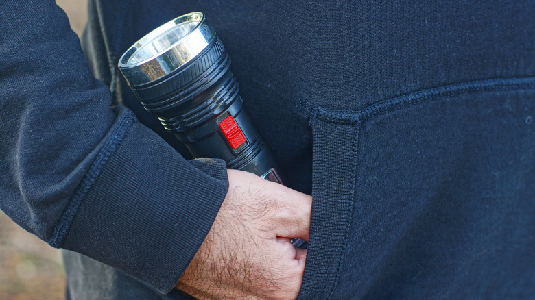 A person holding a bright strobe flashlight in their pocket