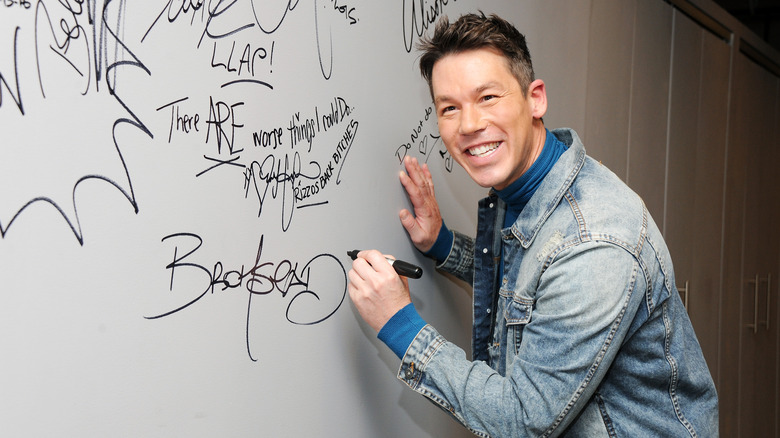 David Bromstad smiles while signing his name on a wall