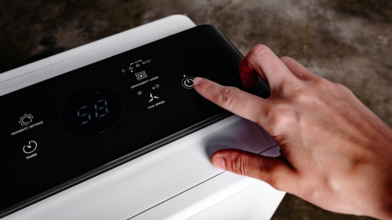 A person's hand is turning on a dehumidifier that's located in a garage