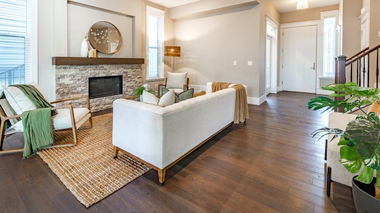 hardwood flooring in living room with light cream upholstered sofa, arm chair, and stone fireplace
