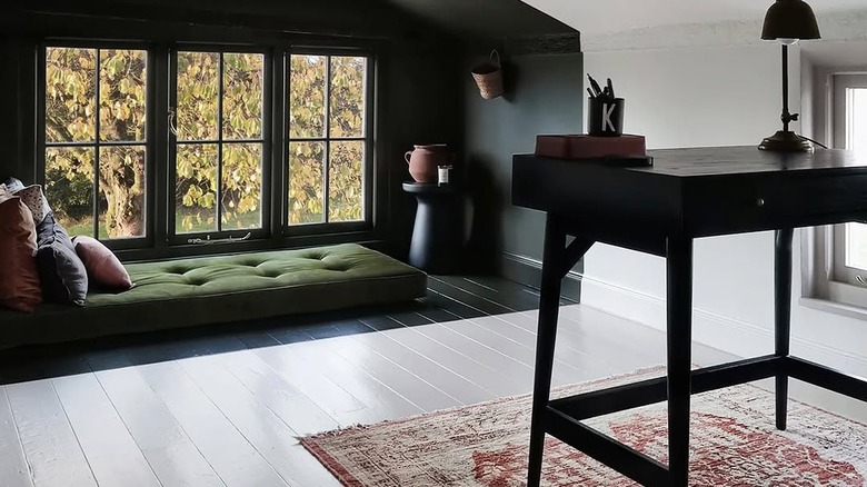 Hardwood floor painted in white with a desk and Persian rug in the foreground of the image and a little nook with the floor painted in dark green and a floor pillow in the background.