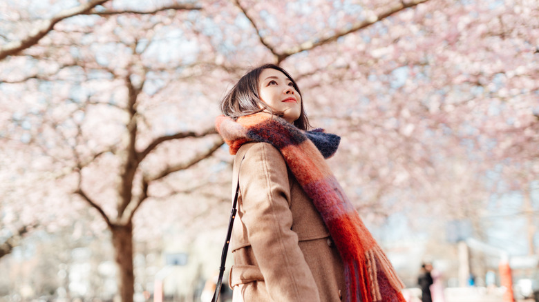 A woman in a coat and scarf walking under a flowering tree