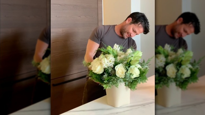 Nate Berkus creating a green and white bouquet arrangement on a marble kitchen countertop.