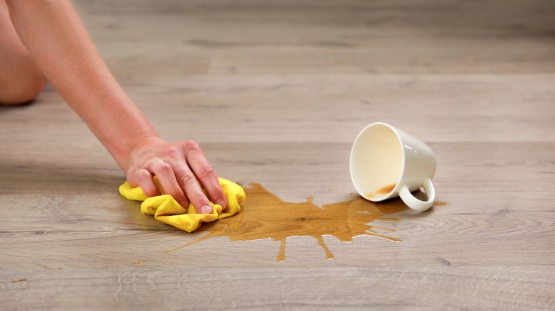 Hand cleaning up coffee spill on floor using a microfiber cloth