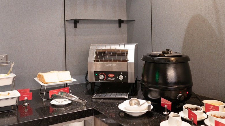 A breakfast buffet with a conveyor toaster in the corner beside a tray of un-toasted bread.