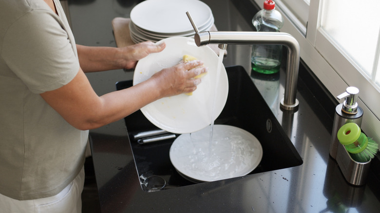 Person handwashing dishes in sink