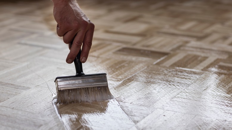 Close-up of a man applying oil to a wood floor with a paint brush
