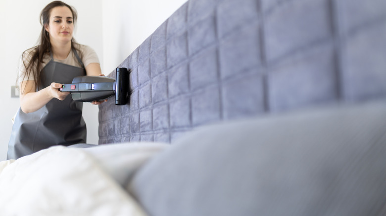 A person vacuuming a velvet-covered headboard