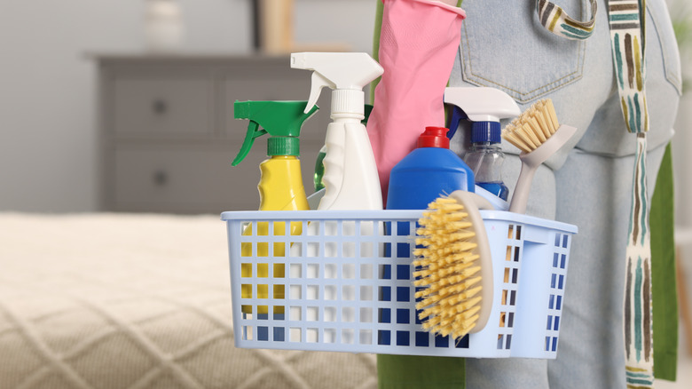 A person holding a basket filled with cleaning supplies in bedroom