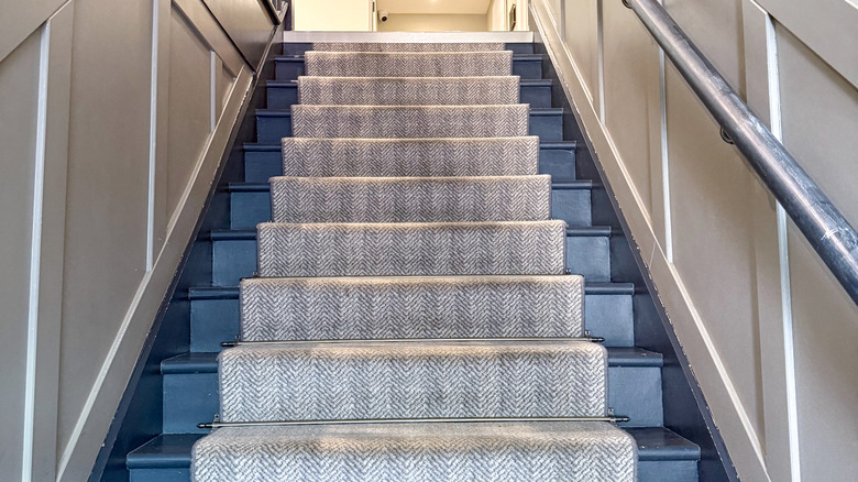 A dark blue painted staircase with greige stair runners and rods