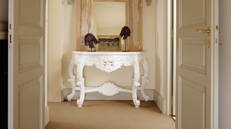 Ornately carved white decorative demilune table set in an entryway