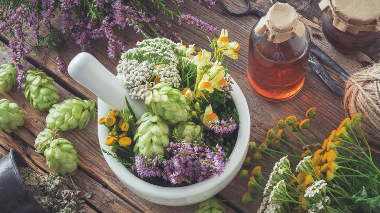 A collection of pretty herbs and flowers in a mortar and pestle on a wooden table