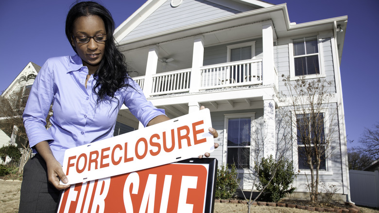 Woman putting foreclosure sign in front of house