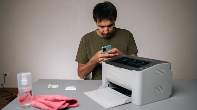 A man looking at instructions on his phone while repairing a printer.