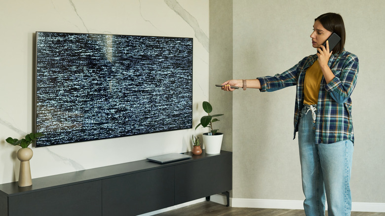 A woman on the phone with tech support attempting to fix a malfunctioning television.
