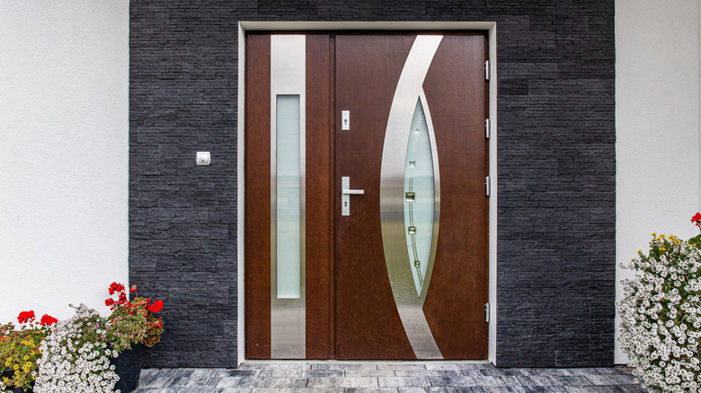 A wooden front door with multicolored glass next to a window with blue trim.