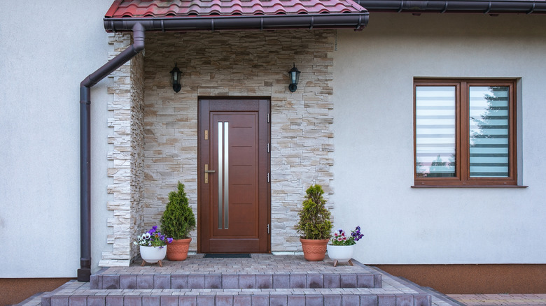 A simple but elegant brown wooden door on a stone house that also has a window with matching wooden trim.