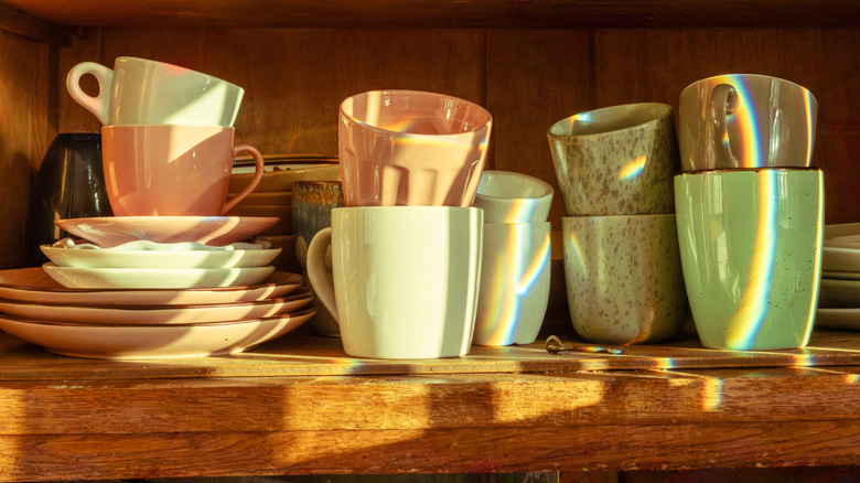 Cluttered coffee mugs on shelf with plates