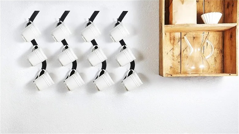 Four curved coffee mug storage racks holding white mugs on white kitchen wall