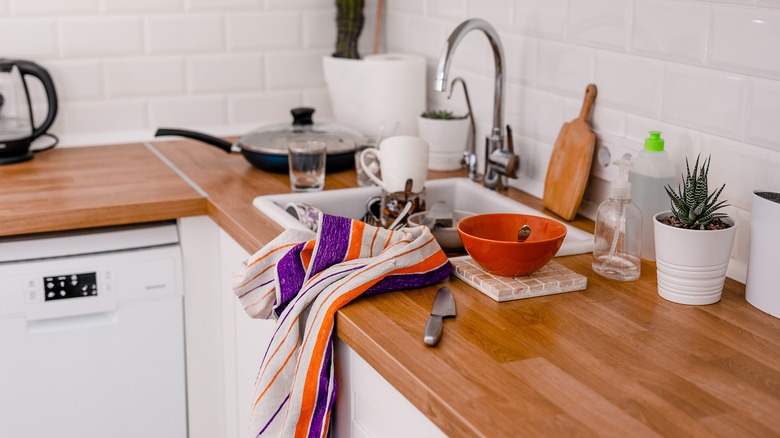 A cluttered kitchen sink with a washcloth and utensils scattered around