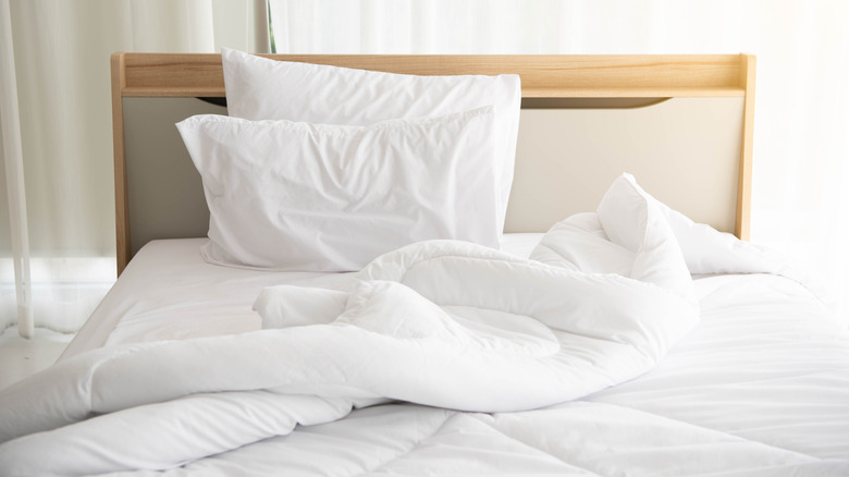 A plain room with a bed and white linens.