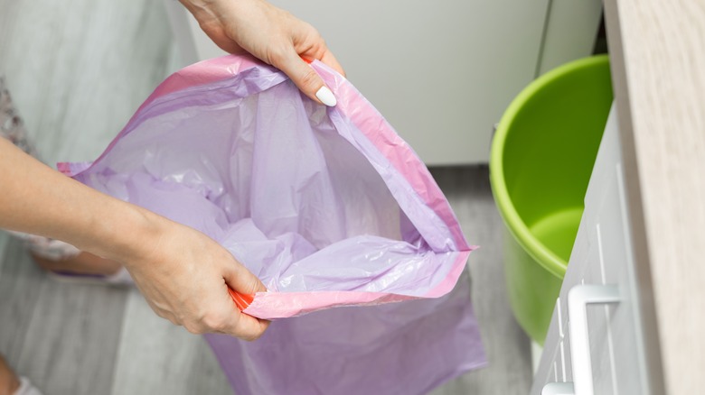 A woman opening up a clear purple trash bag