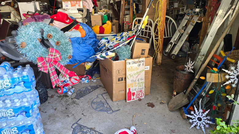 A very messy garage filled with seasonal boxes, bottled water, and junk scattered.
