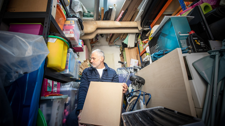 Man trying to store box in over-filled garage.