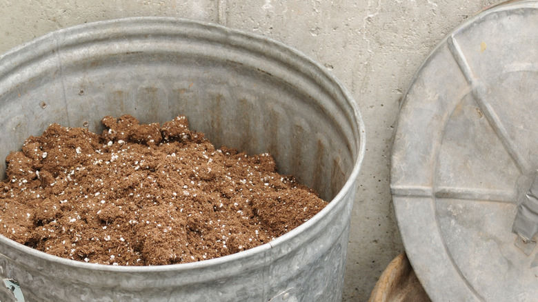 Old potting soil stored in a large metal bin with a tight-fitting lid that has been removed and put to the side.