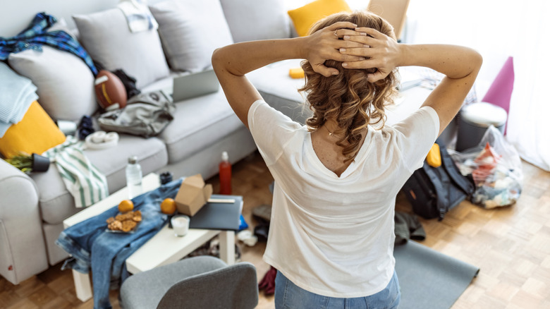 Frustrated woman looking at messy cluttered living room