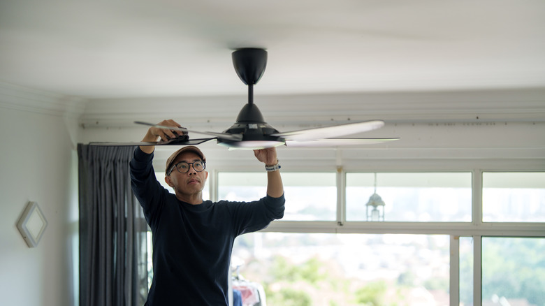 A person carefully cleans the top of a ceiling fan blade