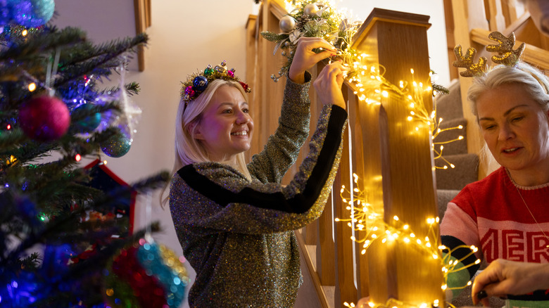 two women hanging Christmas garland and lights on banister