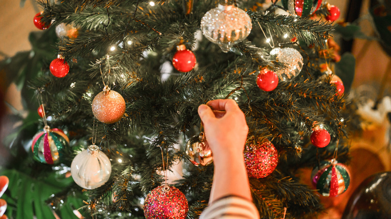 A hand reaching out to hang a Christmas ornament.