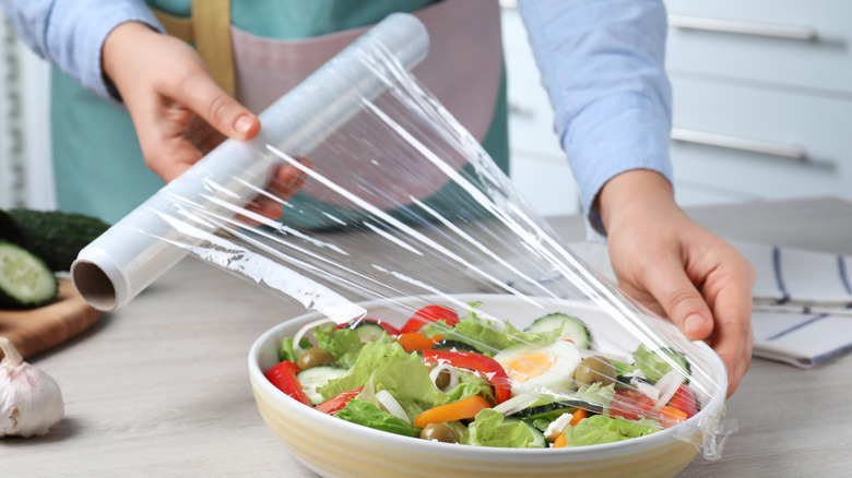 Person putting plastic wrap over salad