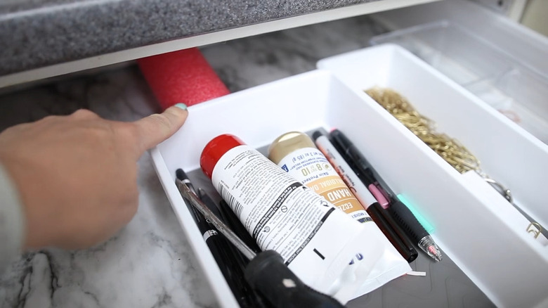 Hand pointing to a pool noodle in a drawer behind a white plastic organizer with paint