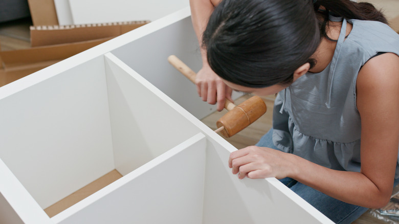Person using a mallet on white cube shelf
