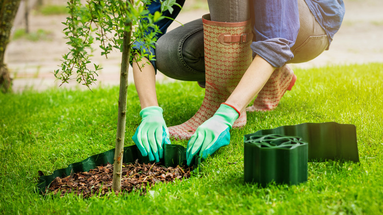 A person wearing gloves installing coiled plastic garden edging