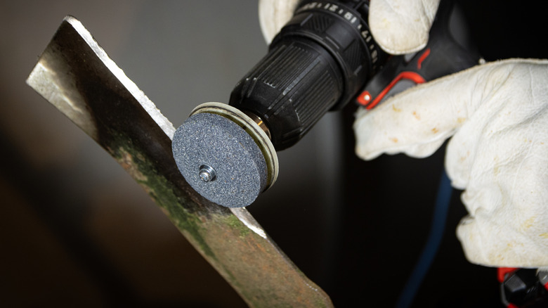 An up close image of someone wearing white gloves using a dremel to sharpen a lawnmower blade.