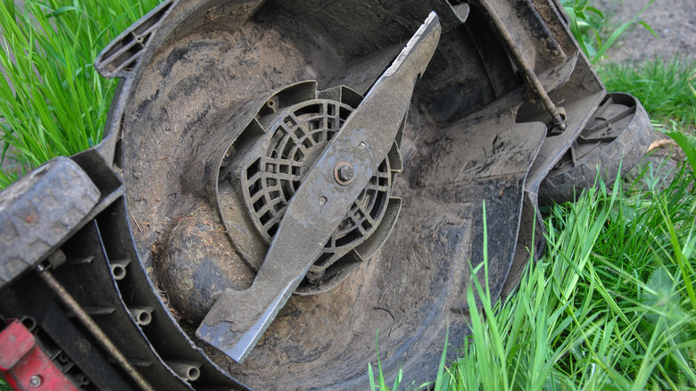 A lawn mower turned on its side exposing a dirty undercarriage.