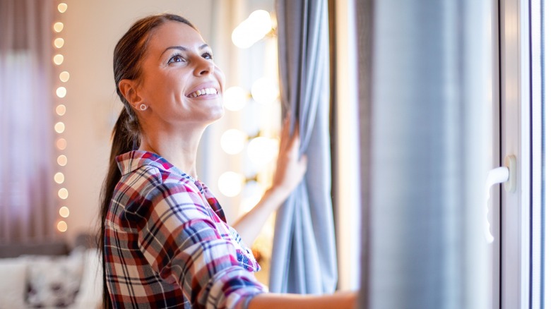 Smiling woman opening up curtains